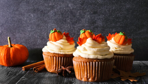 Pumpkin spice cupcakes decorated with white frosting and tiny pumpkins.