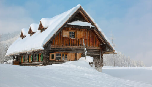 Snow-covered winter cabin in an empty, snowy field.