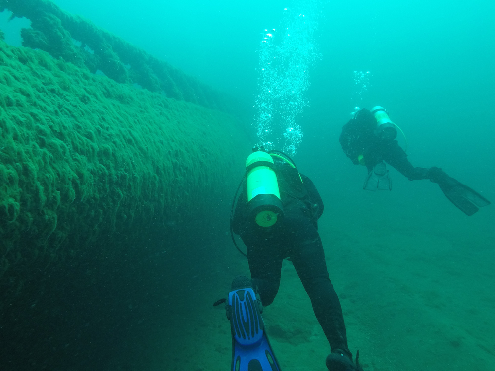 Two scuba divers swim near a shipwreck in the Great Lakes.