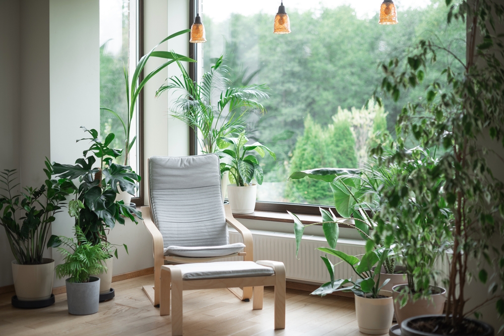 Grey armchair next to a big picture window surrounded by green plants.