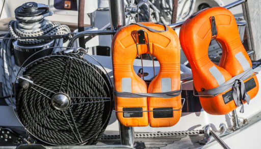 Orange life jackets and a coil of black rope on the back of a boat.