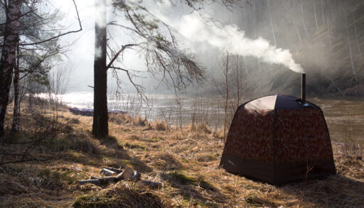 Brown camping sauna tent with an exhaust pipe and steam coming out the top.