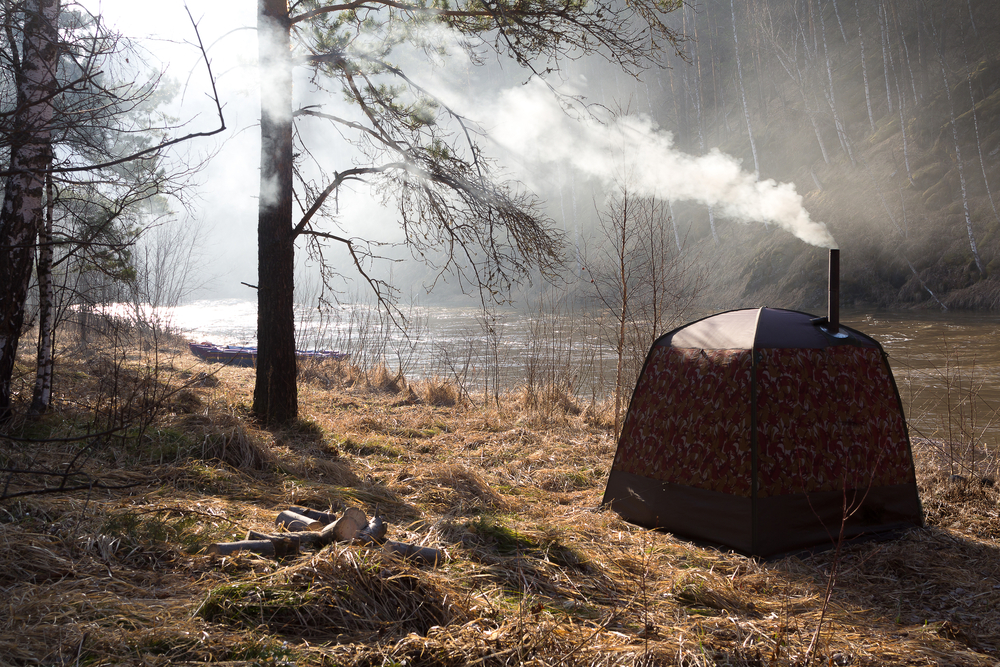 Brown camping sauna tent with an exhaust pipe and steam coming out the top.