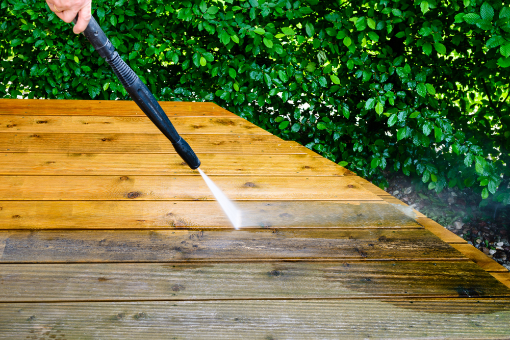Close-up of a person using a pressure washer to clean a deck.