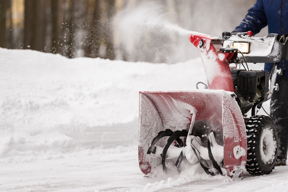 Close-up of a red snow blower clearing snow from a pathway.