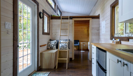 Interior of a tiny home with wood panelling, a small kitchen and a loft.