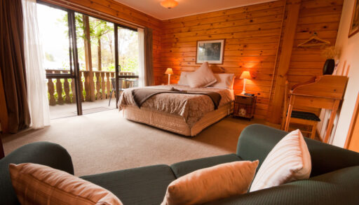 Wood panelled, cozy cabin bedroom with a sliding glass door and chair.