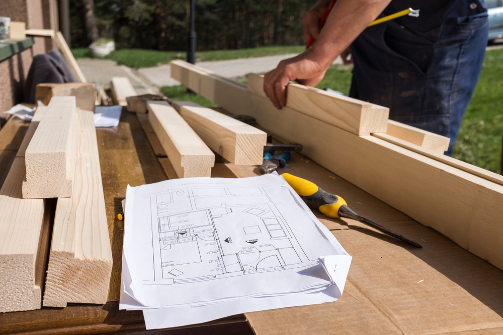 Close-up of a person putting together pieces of wood with a blueprint laying on top.