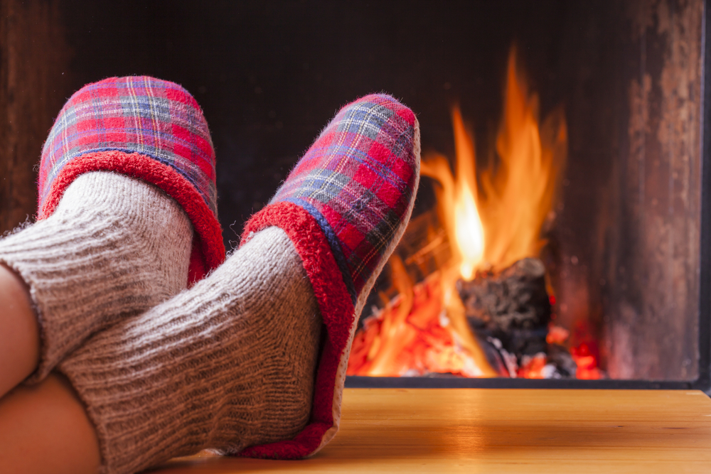 Close-up of a person wearing red plaid slippers in front of a fireplace.