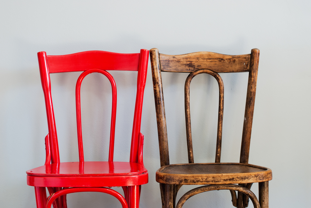Old, wooden chair next to a newly-painted, bright red version of the same chair.