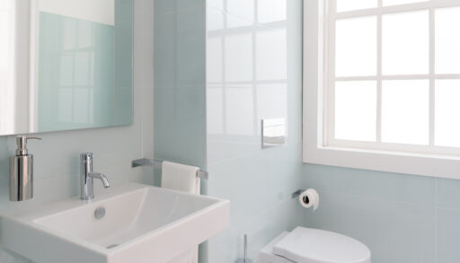 Light-coloured bathroom with light blue tiled walls and a window.