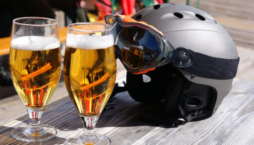 Two glasses of beer in front of a ski helmet on a table.