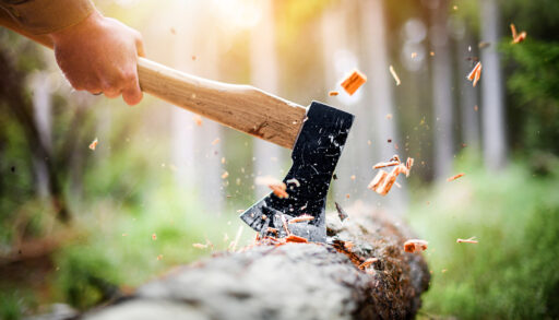 Man using an axe to strike a log with wood chips flying up.