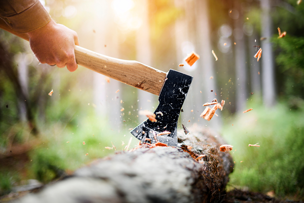 Man using an axe to strike a log with wood chips flying up.