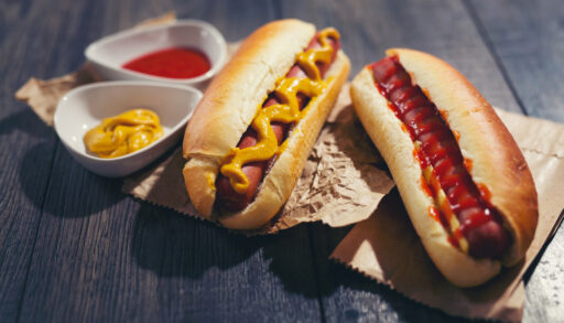Two hot dogs covered in ketchup and mustard.