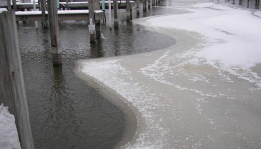 Ice on a lake underneath a row of dock piers.