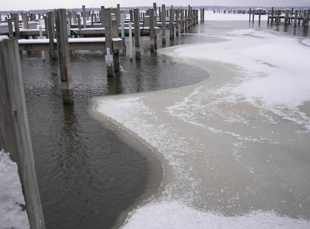 Ice on a lake underneath a row of dock piers.