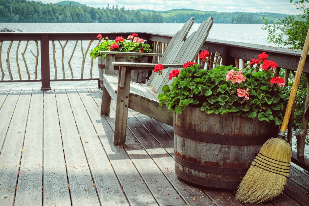 Side view of a wooden deck next to a lake with two Adirondack chairs and wooden flower pots.