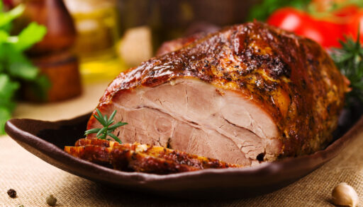 Close-up of a cooked pork roast on a brown plate.