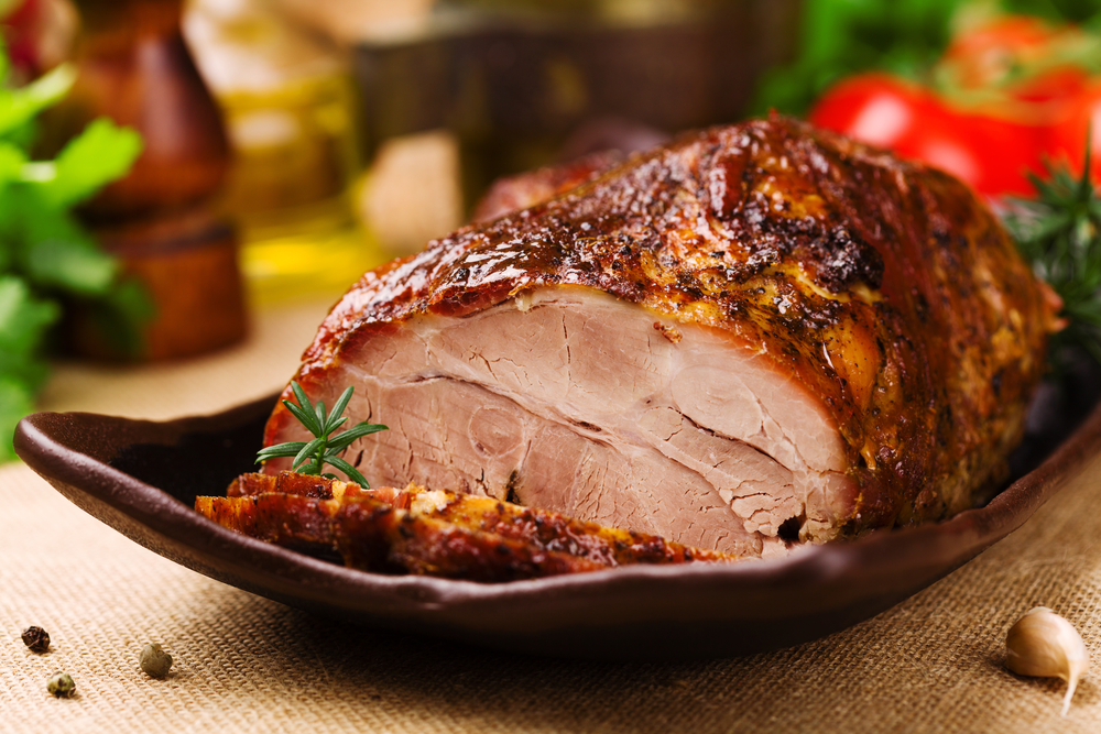Close-up of a cooked pork roast on a brown plate.