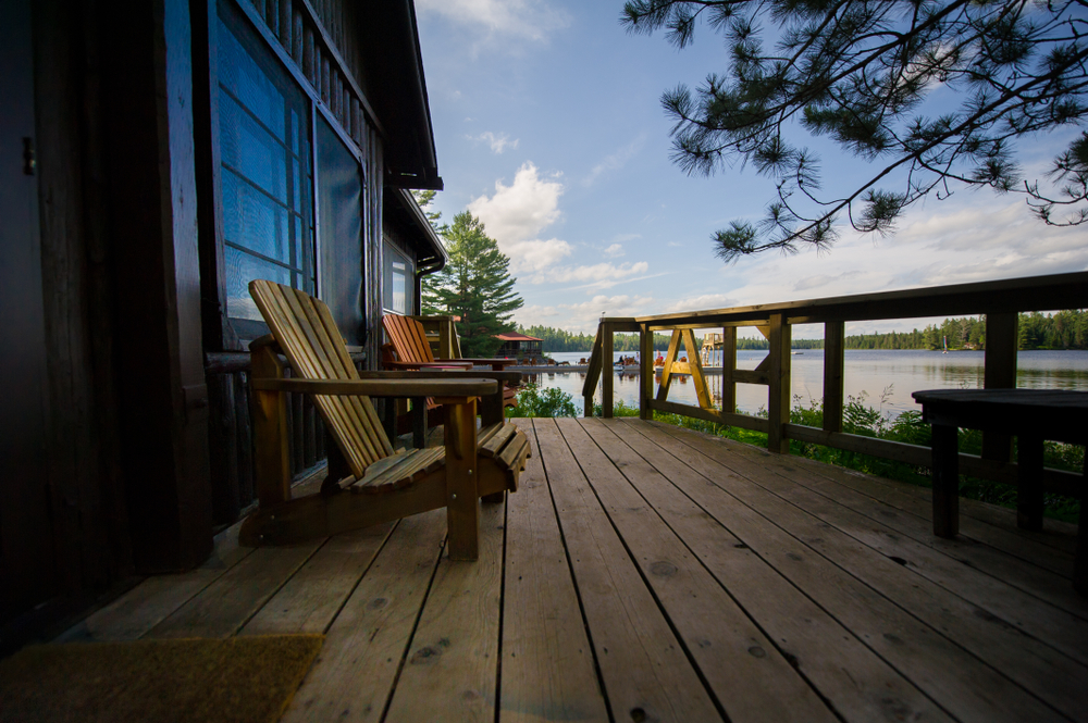 Side view of a deck next to a lake with two Adirondack chairs.