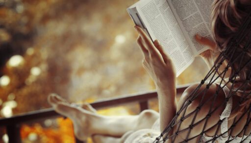 Woman sitting in a hammock reading a book.