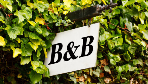 Black and white sign with "B&B" written on it and surrounded by a green hedge.