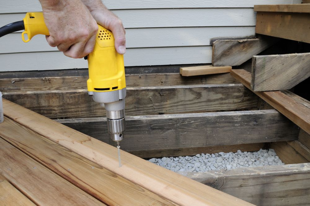 Man using a yellow electric drill to build a deck.