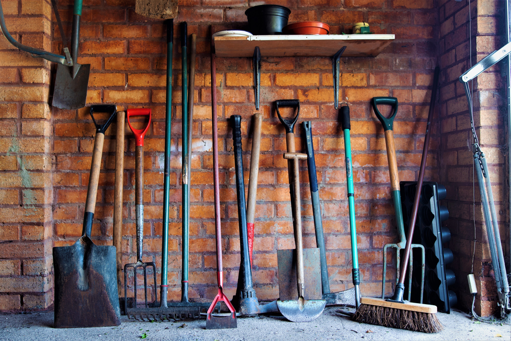 Interior of a brick tool shed with gardening tools lined up along the wall.