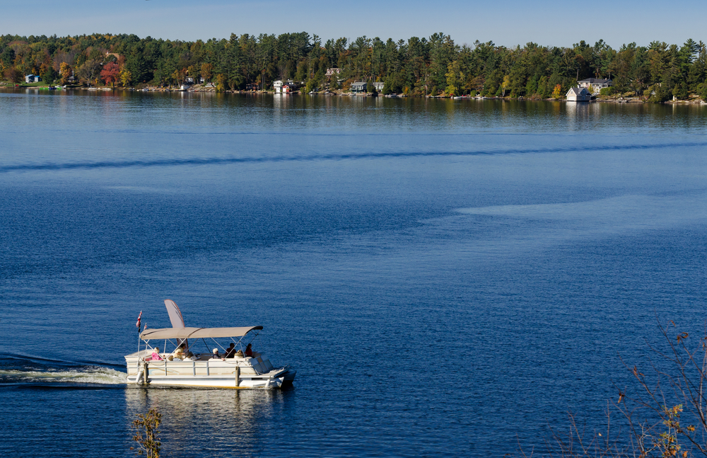 Pontoon boat on a blue lake with a shore covered in trees in the background.