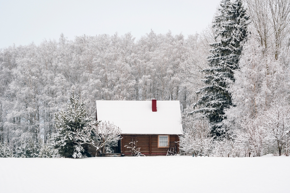 Wood cottage covered in snow and surrounded by snow-covered trees.