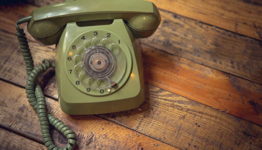Vintage, green rotary telephone sitting on a wooden table.