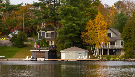 Lakeside cottages with docks and boathouses surrounded by green and orange trees.