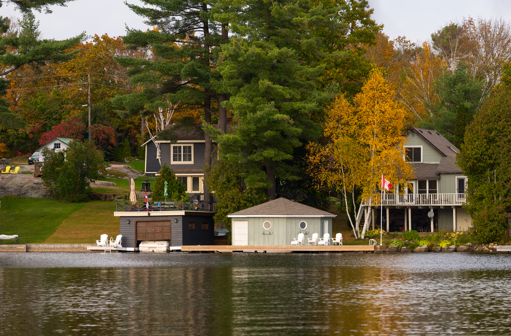 Lakeside cottages with docks and boathouses surrounded by green and orange trees.