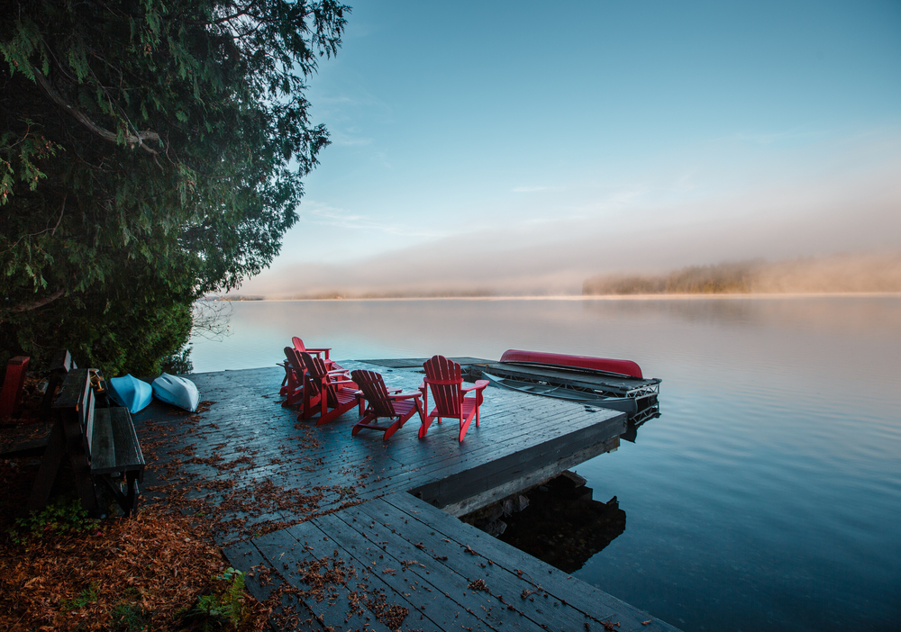 Red Muskoka chairs on a dock with a tree hanging over it.