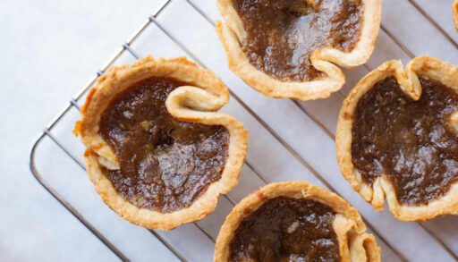 Four butter tarts on a black wire rack.