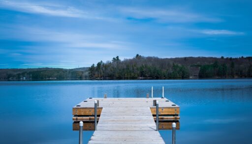 Wooden dock on a lake across from a shoreline covered with trees.