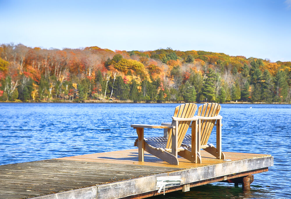 Two Muskoka chairs on a wooden dock on a blue lake.