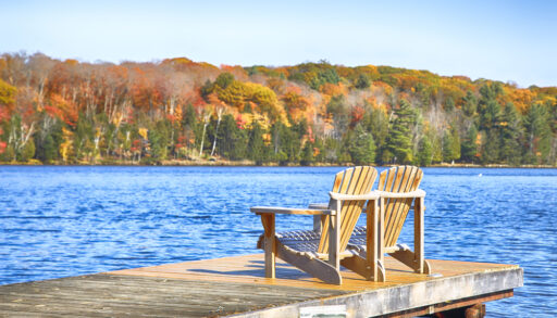 Two Muskoka chairs on a wooden dock on a blue lake.