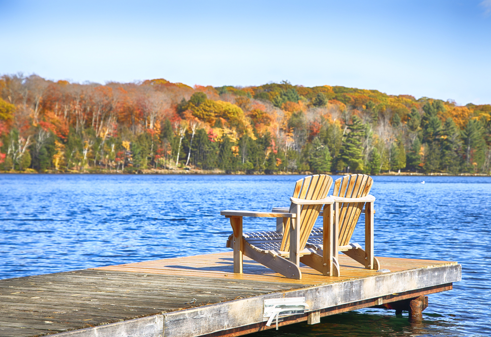 Two Muskoka chairs on a wooden dock on a blue lake.