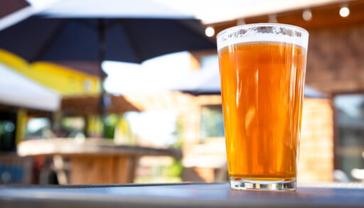Glass of light-coloured beer on a patio table.
