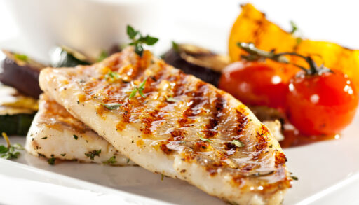 Barbecued fish fillets on a plate with whole tomatoes.
