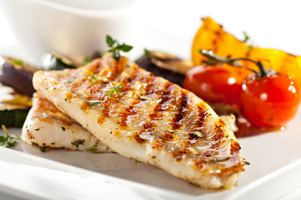 Barbecued fish fillets on a plate with whole tomatoes.