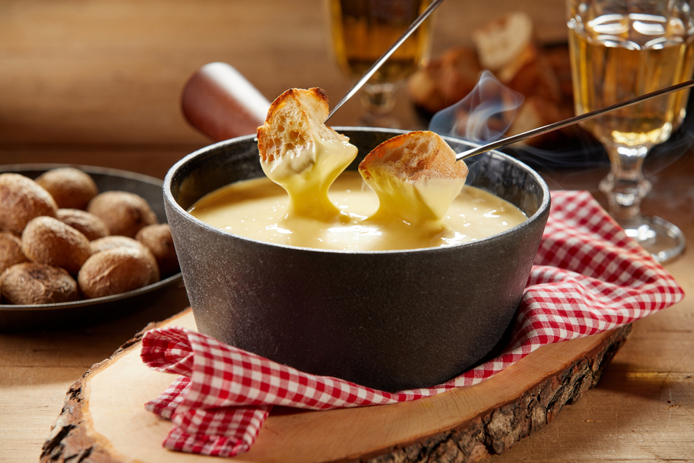 Close-up of bread being dipped in cheese fondue in a cast iron pot.