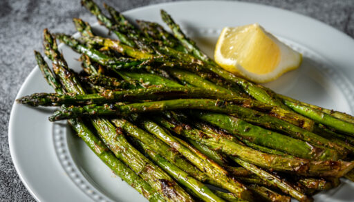 Close-up of grilled asparagus on a white serving plate with a lemon wedge.
