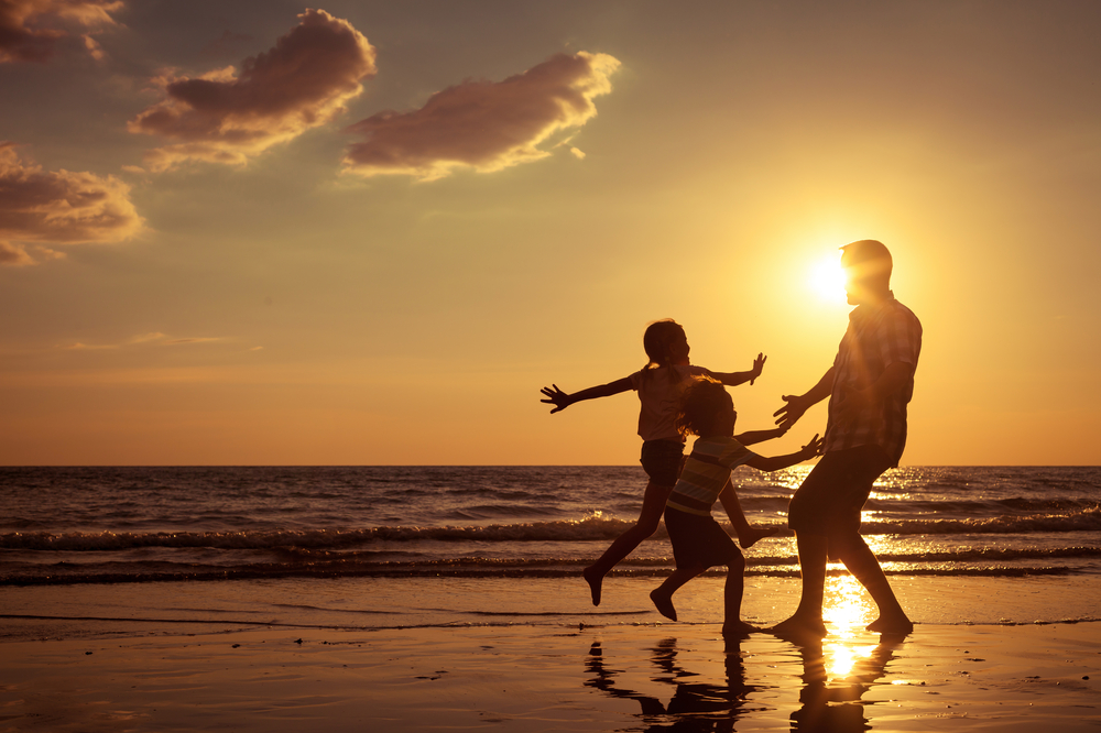 Silhouette of father and children playing on a beach at sunset.