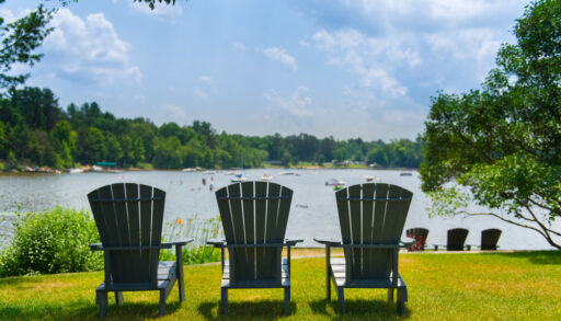 Three Adirondack chairs in front of a lake.