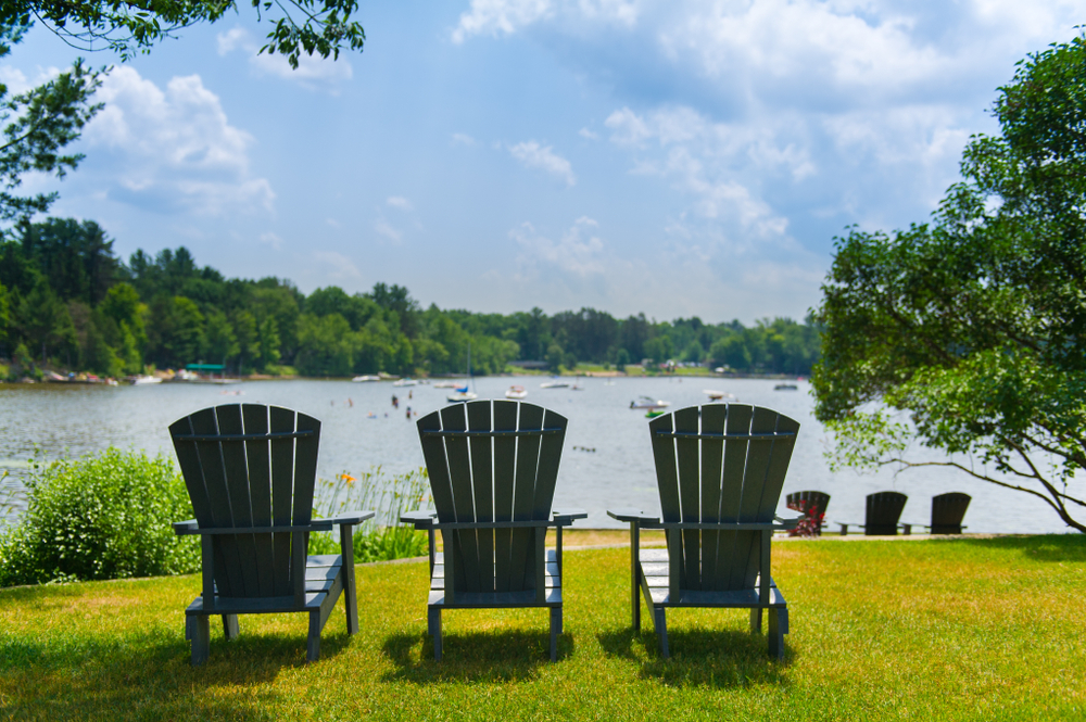 Three Adirondack chairs in front of a lake.