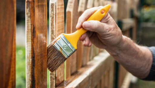 Person painting a wooden picket fence.