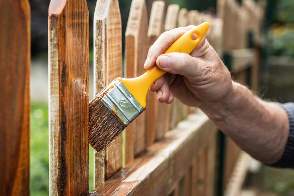 Person painting a wooden picket fence.